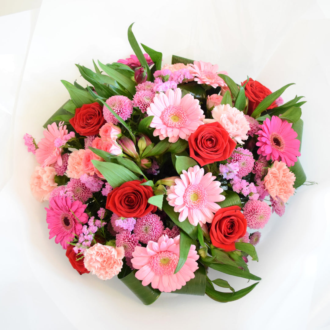 Deene Hand-Tied Bouquet - Magnolia the Florist Indulge in luxury and romance with our Deene Hand-Tied Bouquet. This exquisite bouquet features a stunning array of flowers, including Red and Pink roses, alstroemeria, carnations, and chrysanthemums and adorned with delicate greenery. Hand-tied with care and presented in one of our signature box bags, let the beauty of these blooms bring joy to your loved ones! For scale purposes, our hand-tied bags are 18cm(w) x 25cm(H).  1