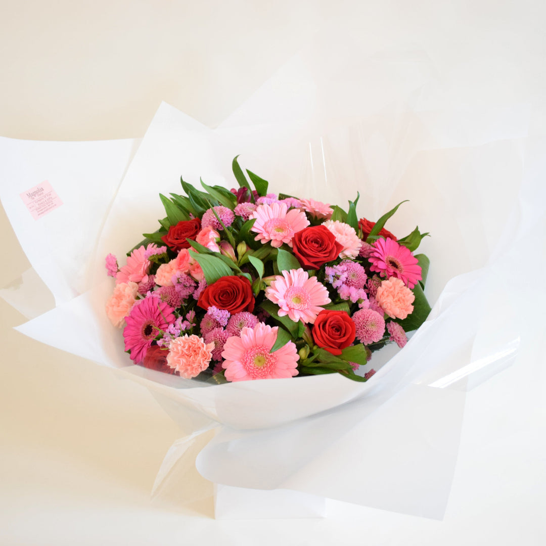 Deene Hand-Tied Bouquet - Magnolia the Florist Indulge in luxury and romance with our Deene Hand-Tied Bouquet. This exquisite bouquet features a stunning array of flowers, including Red and Pink roses, alstroemeria, carnations, and chrysanthemums and adorned with delicate greenery. Hand-tied with care and presented in one of our signature box bags, let the beauty of these blooms bring joy to your loved ones! For scale purposes, our hand-tied bags are 18cm(w) x 25cm(H).  2