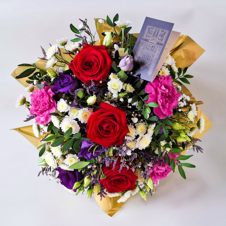 Dainty Belvedere Arrangement - Magnolia the Florist Belvedere blends rich red roses with cerise carnations, white chrysanthemum, purple lisianthus, limonium, gyp and pistache to create a romantic, luxurious floral arrangement. Presented in our Magnolia‑branded box and arranged in floral foam for long‑lasting freshness. For scale purposes, our branded box is 15cm(h) x 12cm(w) x 12cm(d), giving an overall size of approximately 25cm(h) x 18cm(w).  2