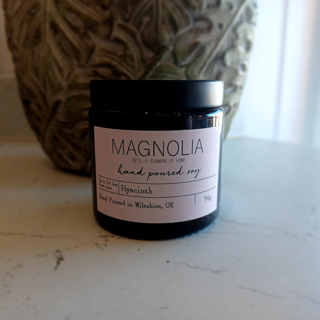 Hyacinth Scented Candle - 96g - Magnolia the Florist Indulge in the luxurious aroma of our hyacinth-scented jar candle. Crafted with a delicate blend of essential oils, this candle fills the air with the enchanting fragrance of fresh hyacinths. Perfect for creating a sophisticated and exclusive ambience in any space. Enjoy the aromatic benefits while enhancing any room with a touch of elegance, made with a professional blend of scented oil & emollient wax balm.  1