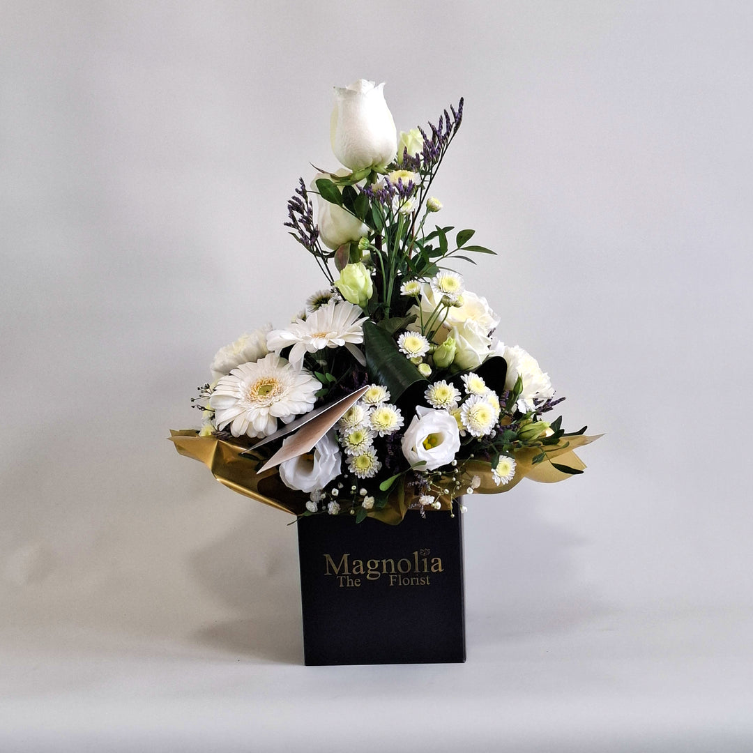 Iona Arrangement - Magnolia the Florist Iona is a pure and elegant floral arrangement featuring white roses, white germini, white carnations, white chrysanthemum, white lisianthus, folded aspidistra, limonium, gyp and pistache. Presented in our Magnolia branded box and arranged in floral foam for long lasting freshness. For scale purposes, our branded box is 15cm (h) x 12cm (w) x 12cm (d), giving an overall size of approximately 35cm (h) x 18cm (w).  1