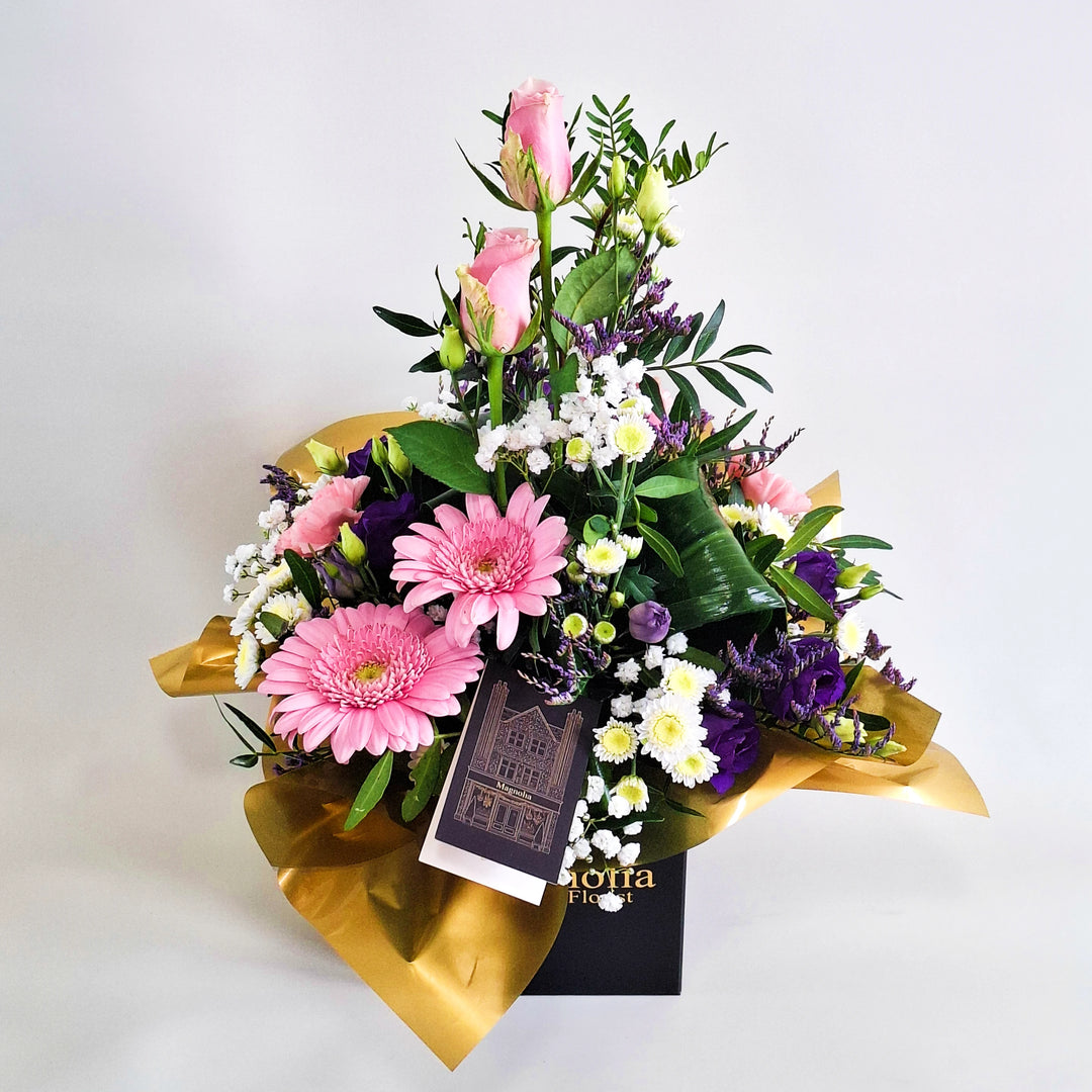 Islay Arrangement - Magnolia the Florist Islay is a soft, feminine floral arrangement crafted with pink roses, pink carnations, pink germini, white chrysanthemum, purple lisianthus, folded aspidistra, limonium, gyp and pistache. Presented in our Magnolia‑branded box and arranged in floral foam for long‑lasting freshness. For scale purposes, our branded box is 15cm (h) x 12cm (w) x 12cm (d), giving an overall size of approximately 35cm (h) x 18cm (w).  3