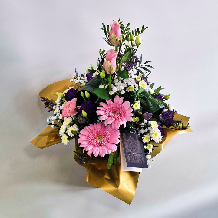 Islay Arrangement - Magnolia the Florist Islay is a soft, feminine floral arrangement crafted with pink roses, pink carnations, pink germini, white chrysanthemum, purple lisianthus, folded aspidistra, limonium, gyp and pistache. Presented in our Magnolia‑branded box and arranged in floral foam for long‑lasting freshness. For scale purposes, our branded box is 15cm (h) x 12cm (w) x 12cm (d), giving an overall size of approximately 35cm (h) x 18cm (w).  2