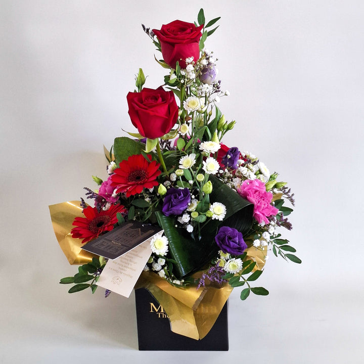 Jura Arrangement - Magnolia the Florist Jura is a dramatic, structured floral arrangement featuring red germini, red roses, cerise carnations, white chrysanthemum, purple lisianthus, folded aspidistra, limonium, gyp and pistache. Presented in our Magnolia‑branded box and arranged in floral foam for long‑lasting freshness. For scale purposes, our branded box is 15cm (h) x 12cm (w) x 12cm (d), giving an overall size of approximately 35cm (h) x 18cm (w).  3