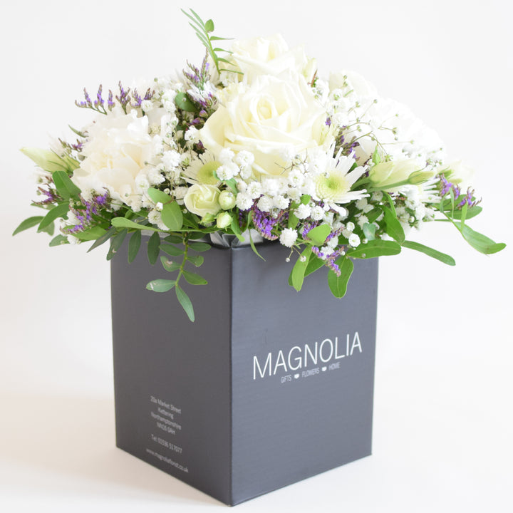 Dainty Kew Arrangement - Magnolia the Florist The Kew Arrangement from Magnolia the Florist, features a stunning mix of white florals with a hint of purple, including roses, carnations, lisianthus, gyp, chrysanthemum and limonium, all arranged in floral foam. Presented in a signature box, it makes a beautiful and sophisticated gift for any occasion. For scale purposes, the box container measures approximately 15cm x 12cm x 12cm, giving the overall arrangement size of 25cm h x 18cm w approximately.  3