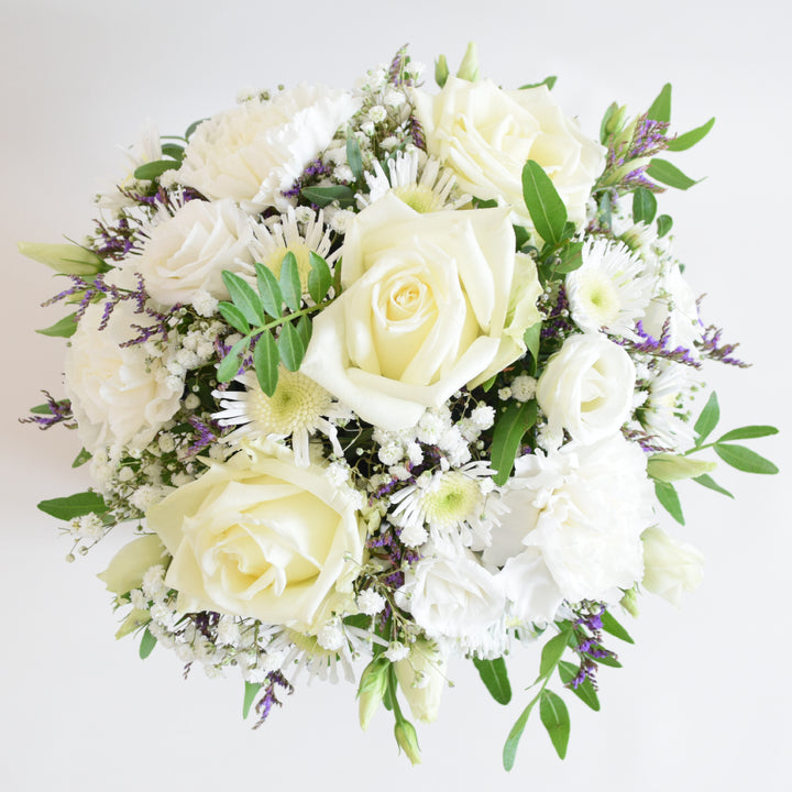 Dainty Kew Arrangement - Magnolia the Florist The Kew Arrangement from Magnolia the Florist, features a stunning mix of white florals with a hint of purple, including roses, carnations, lisianthus, gyp, chrysanthemum and limonium, all arranged in floral foam. Presented in a signature box, it makes a beautiful and sophisticated gift for any occasion. For scale purposes, the box container measures approximately 15cm x 12cm x 12cm, giving the overall arrangement size of 25cm h x 18cm w approximately.  2