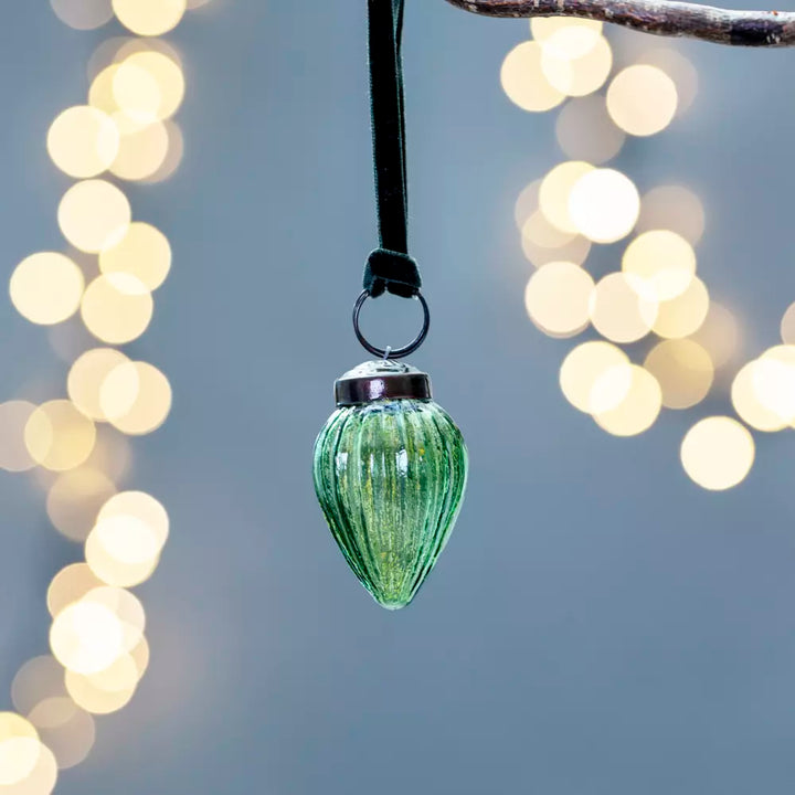 Ribbed Gourd Decoration Green With Velvet Loop 5x3cm - Magnolia the Florist Presented in an alluring clear green hue, this gourd shaped bauble looks stunning either adorning a tree or strung on a branch for a contemporary twist. With vertical ribs, light will play off the surface for amplified sparkle. The soft velvet loop in a complementary colour completes the look. Dimensions: 3 × 5 cm - Glass  1
