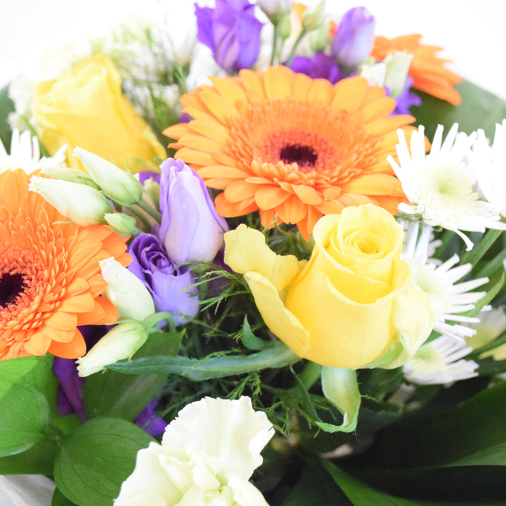 Savoy Hand-Tied Bouquet - Magnolia the Florist With vibrant hues of yellow, orange, green, and purple, the Savoy Hand-Tied Bouquet from Magnolia the Florist, is a stunning mix of Roses, Mini Gerbera, Lisianthus, Carnations, Chrysanthemums, and foliage. Expertly arranged in our signature box bags, this aqua bouquet is sure to brighten any space. Perfect for any occasion, bring a touch of nature&