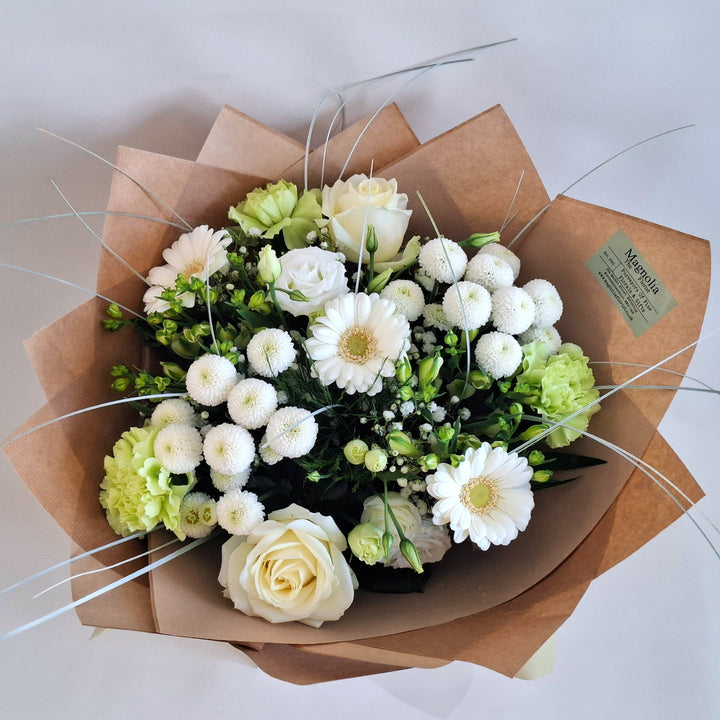 Sibbertoft Bouquet - Magnolia the Florist The Sibbertoft Bouquet showcases a sophisticated hand-tied arrangement of fresh Germini, Carnations, Eustoma, Roses, Alstroemeria, Chrysanthemums, and Gypsophila, elegantly presented in white and green tones. Enhanced with lush greenery, this bouquet offers a fresh, timeless appeal suited for both formal and intimate settings.  2