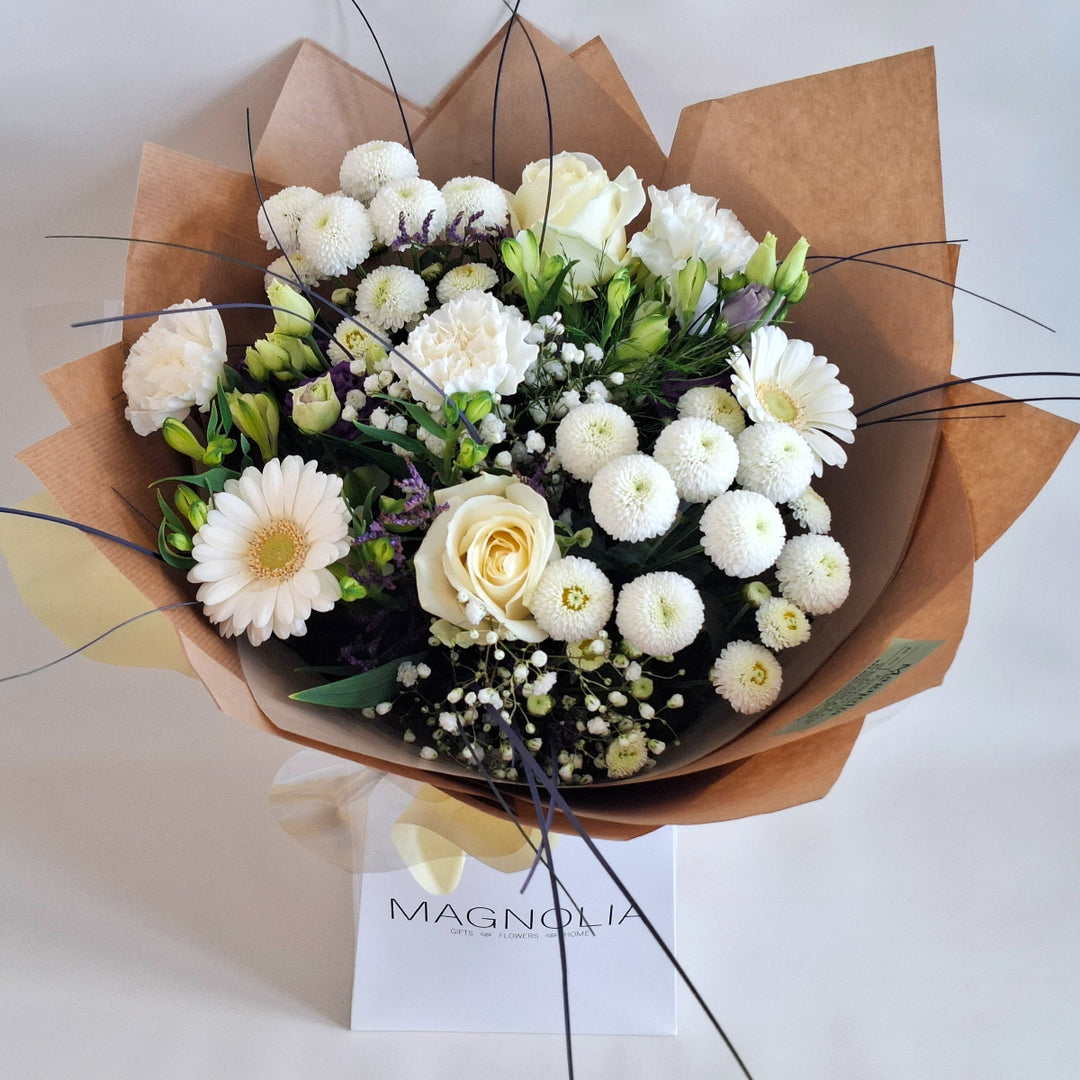 Wadenhoe Bouquet - Magnolia the Florist The Wadenhoe Bouquet is a meticulously hand-tied arrangement blending fresh Germini, Roses, Chrysanthemums, Eustoma, Alstroemeria, Carnations, Gypsophila, and Statice in elegant white and purple hues. Accented with lush greenery, it offers a sophisticated balance of texture and color, ideal for expressing refined taste and appreciation. Perfect for elevating any occasion with timeless floral beauty.  1
