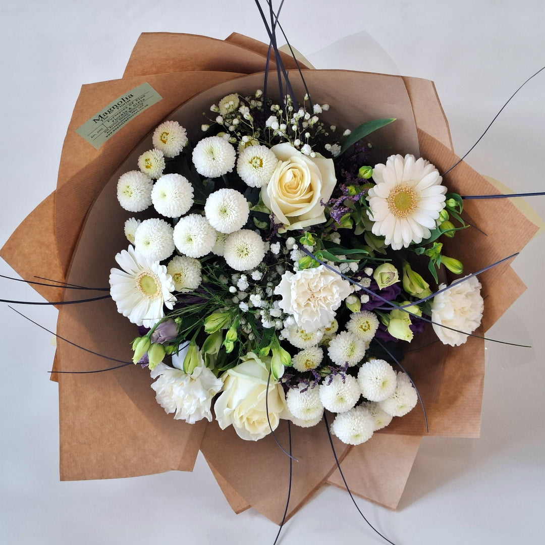 Wadenhoe Bouquet - Magnolia the Florist The Wadenhoe Bouquet is a meticulously hand-tied arrangement blending fresh Germini, Roses, Chrysanthemums, Eustoma, Alstroemeria, Carnations, Gypsophila, and Statice in elegant white and purple hues. Accented with lush greenery, it offers a sophisticated balance of texture and color, ideal for expressing refined taste and appreciation. Perfect for elevating any occasion with timeless floral beauty.  2