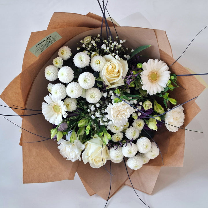 Wadenhoe Bouquet - Magnolia the Florist The Wadenhoe Bouquet is a meticulously hand-tied arrangement blending fresh Germini, Roses, Chrysanthemums, Eustoma, Alstroemeria, Carnations, Gypsophila, and Statice in elegant white and purple hues. Accented with lush greenery, it offers a sophisticated balance of texture and color, ideal for expressing refined taste and appreciation. Perfect for elevating any occasion with timeless floral beauty.  2