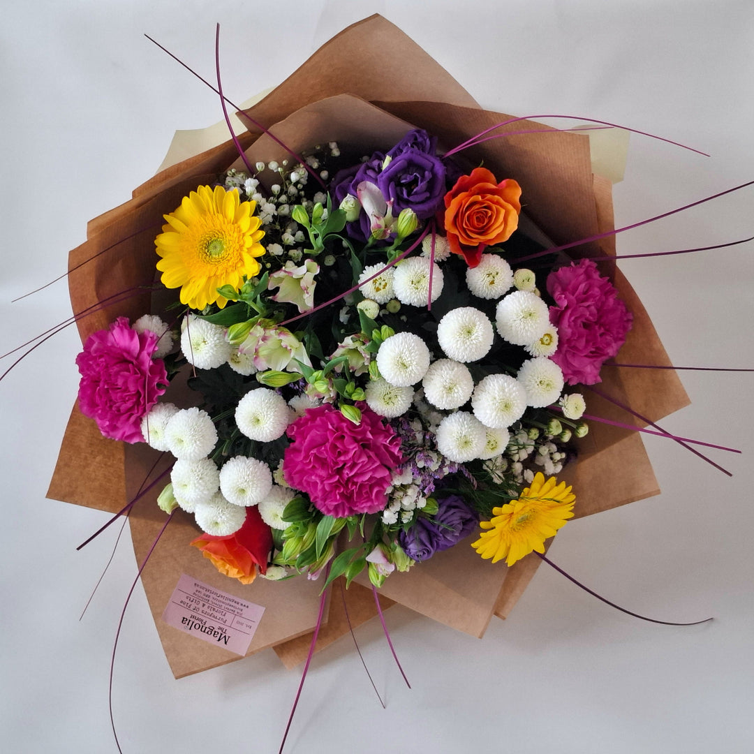 Yarwell Bouquet - Magnolia the Florist The Yarwell Bouquet is an expertly crafted hand-tied arrangement blending Roses, Germini, Chrysanthemums, Eustoma, Gyp, Alstroemeria, Carnations, and Statice. Its vibrant palette of yellow, orange, white, pink, cerise, and purple tones is beautifully complemented by fresh greenery, creating a harmonious and elegant floral display perfect for any occasion.  2
