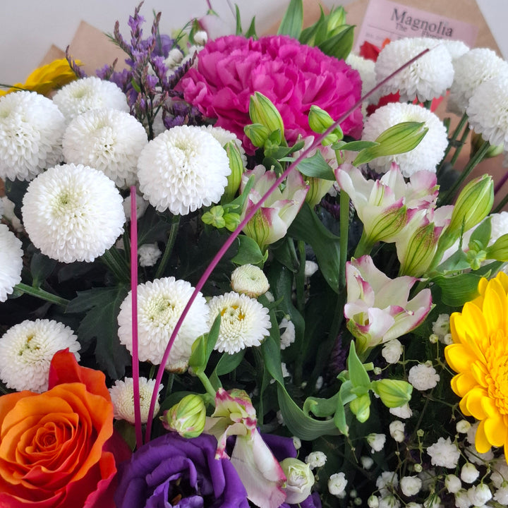 Yarwell Bouquet - Magnolia the Florist The Yarwell Bouquet is an expertly crafted hand-tied arrangement blending Roses, Germini, Chrysanthemums, Eustoma, Gyp, Alstroemeria, Carnations, and Statice. Its vibrant palette of yellow, orange, white, pink, cerise, and purple tones is beautifully complemented by fresh greenery, creating a harmonious and elegant floral display perfect for any occasion.  3