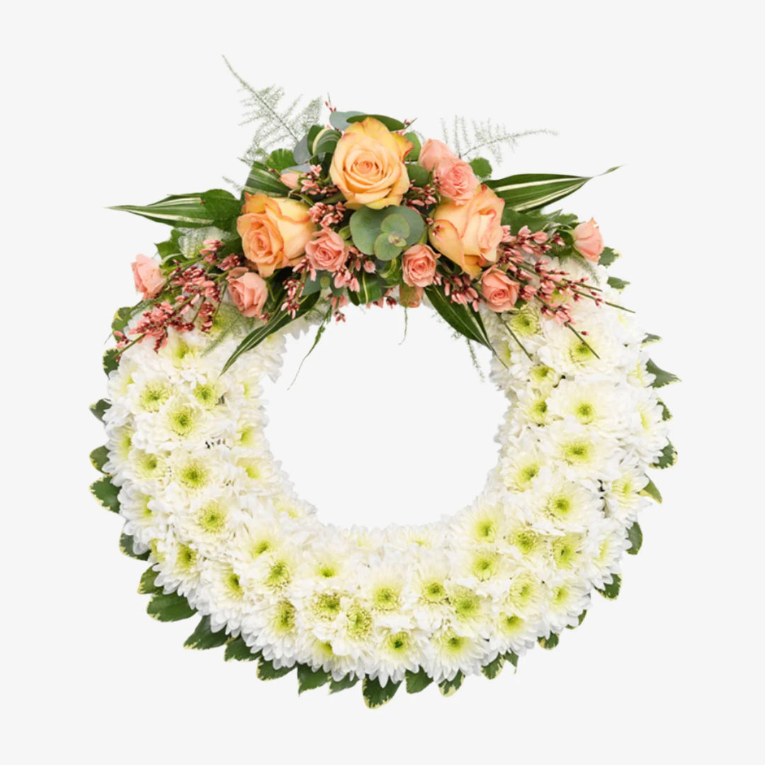 Based Wreath - Magnolia the Florist A classic circular wreath covered with a mass of white Double Spray Chrysanthemums and finished with a spray of coloured flowers. This image shows a selection of peach-toned flowers, the spray can be changed to other colour options. Please select from the options below. If you cannot find what you want on our site, please call our sales team, we're always happy to assist you. This item requires 3 days notice to order.  1
